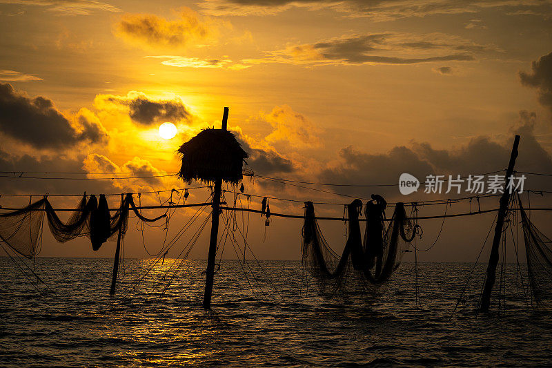 在日出期间，越南Tra Vinh省的渔民在海上拉鱼竿上的渔网的剪影，当地人称之为Day hang khoi。